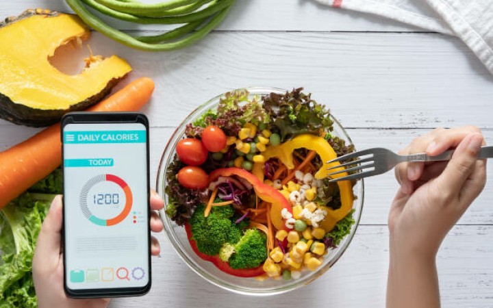 Ilustrasi: Penghitung kalori di layar smartphone di meja makan dengan salad, jus buah, roti, dan sayuran segar