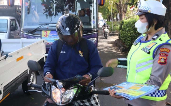 Salah seorang Polwan membagikan selebaran terkait keselamatan berlalu lintas kepada seorang warga yang melintas di salah satu ruas jalan di Denpasar, Bali, Senin (foto: gembali/ antara)
